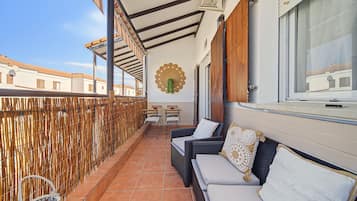 A balcony with wicker furniture, a woven fence, and a view of neighboring buildings.