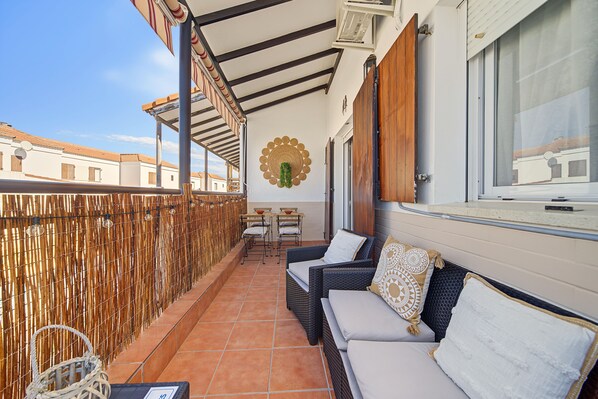 A balcony with wicker furniture, a woven fence, and a view of neighboring buildings.