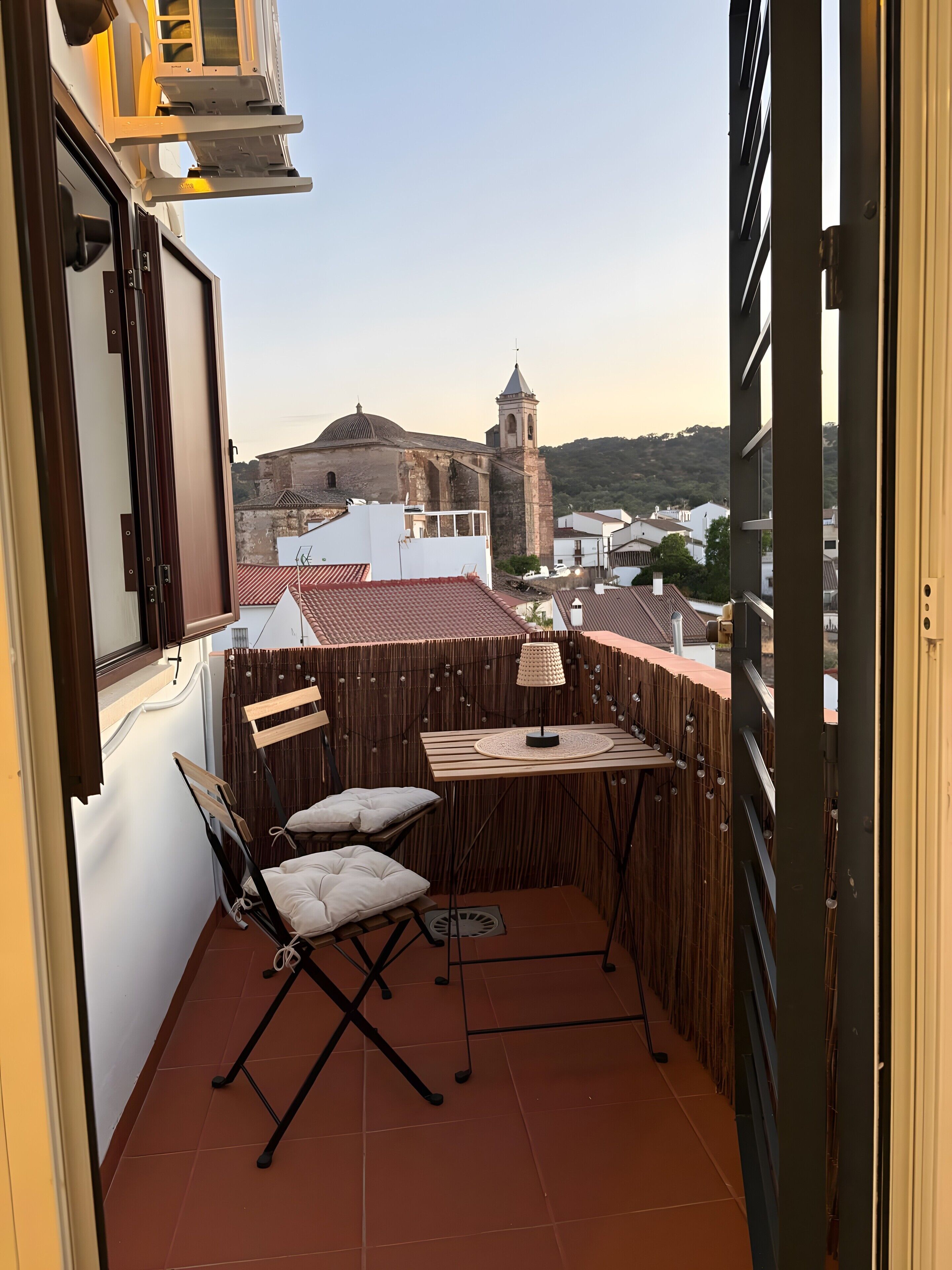 Een balkon met een tafel en stoelen, uitzicht op een historisch gebouw, en een betegelde vloer.