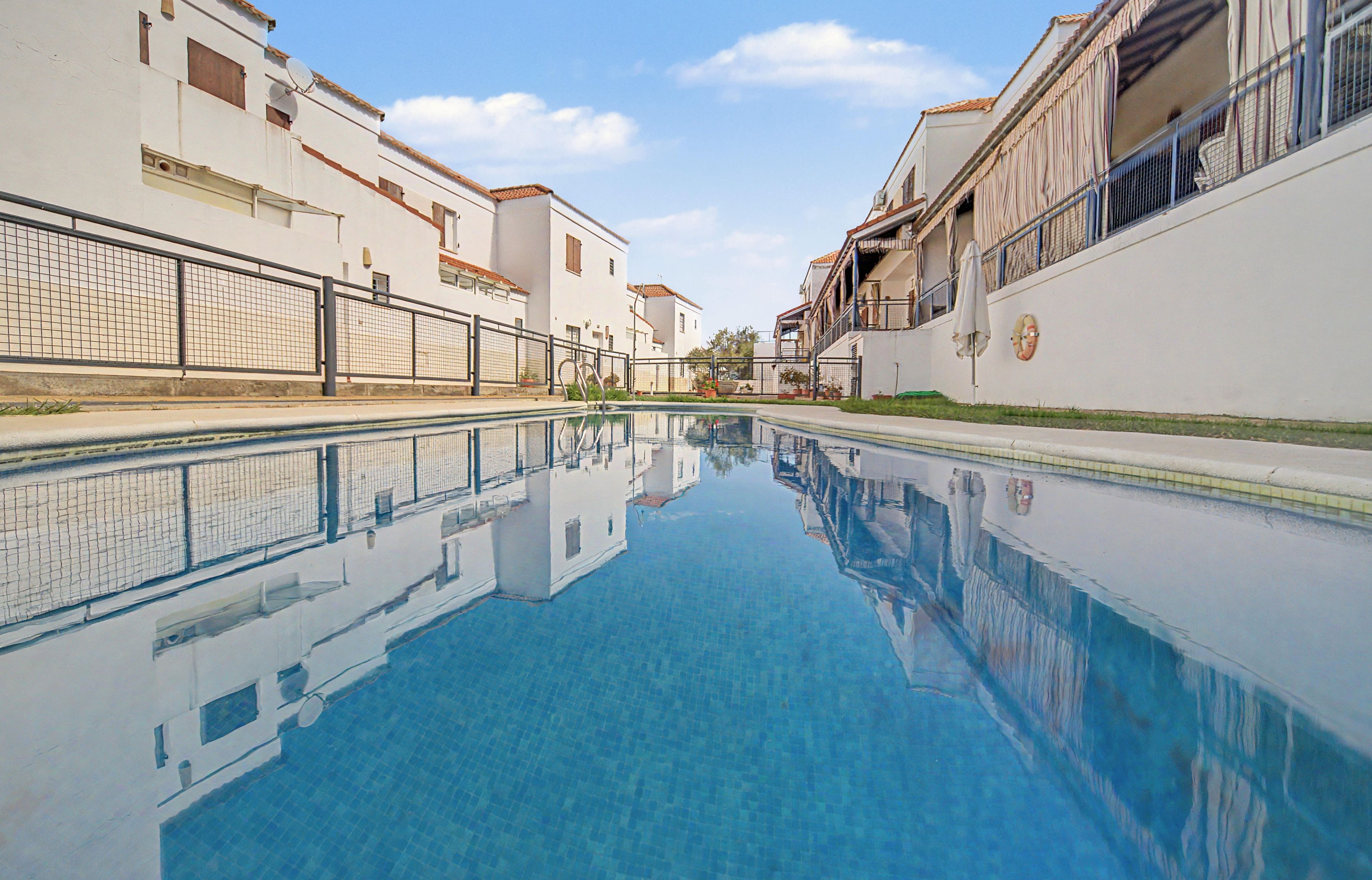 Une piscine à l’eau d’un bleu cristallin, entourée de bâtiments blancs dotés de balcons et protégée par une clôture.