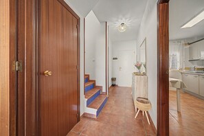 A hallway with a wooden door, a staircase, and a kitchen area.