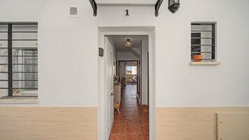 Un pasillo con piso de baldosas que conduce a una puerta, un cartel con el número '1' arriba y una ventana con una planta a la derecha.
