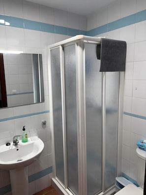 Une salle de bain avec un lavabo blanc, un miroir, un espace douche et des toilettes.