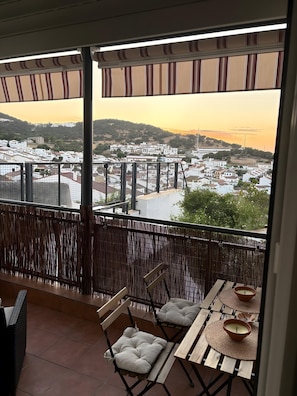Un balcon offrant une vue sur la ville et les collines, avec une table, des chaises et un vase décoratif.