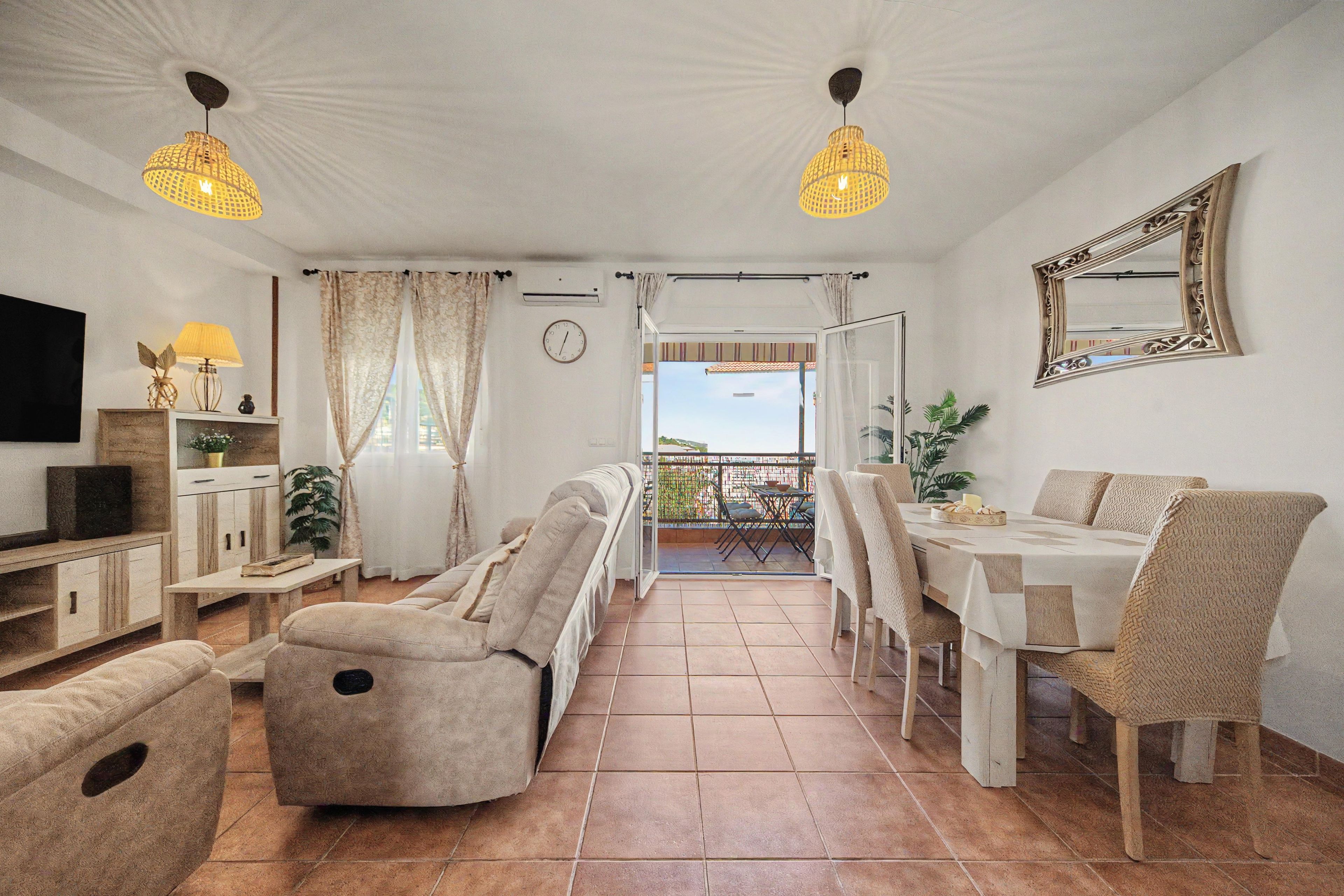 Amplia sala de estar con sofá, mesa de comedor y sillas, un balcón con vistas y un televisor en la pared.