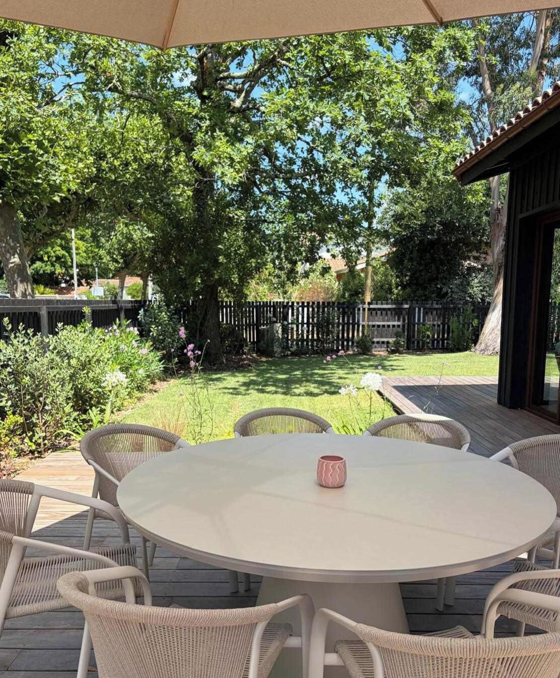 Une terrasse extérieure avec une table ronde et des chaises en osier, entourée d’une plateforme en bois et d’une clôture en bois.