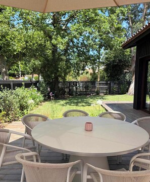 An outdoor patio with a round table and wicker chairs, surrounded by a wooden deck and a wooden fence. - Villa La Perle by HILO Collection (Andernos-les-Bains)