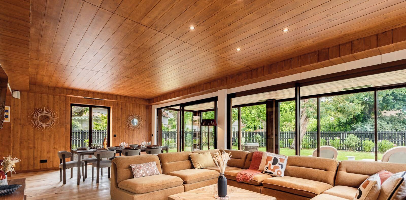 A spacious living area with a wooden ceiling, large windows, and a modern sofa set.