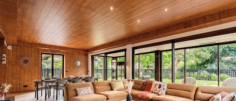 A spacious living area with a wooden ceiling, large windows, and a modern sofa set.