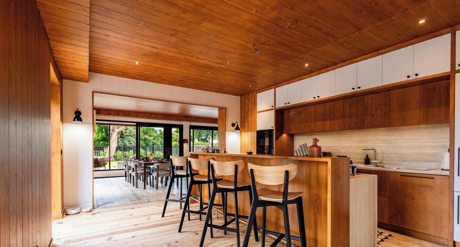 A modern kitchen with wooden cabinets, a central island with bar stools, and a large window providing a view of the outdoors.