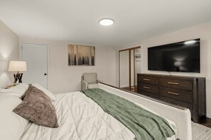 Een slaapkamer met een bed, een dressoir, een televisie en een schilderij aan de muur.