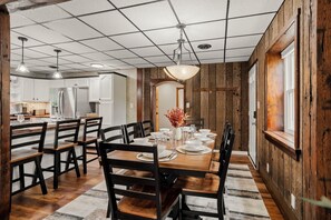 Un comedor con mesa de madera dispuesta para cuatro, rodeada de sillas, y una cocina al fondo.