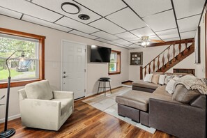 A living room with a sofa, a chair, a TV, a staircase, and a window with a view. - Lantz Retreat  Hot Tub • Spacious Deck (Lebanon)