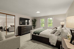 Un dormitorio moderno con una cama grande, un aparador, un televisor y una ventana con vistas a zonas verdes.