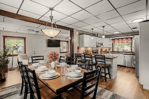 A modern kitchen with white cabinets, a wooden dining table set for six, and a large island with a sink. - Lantz Retreat  Hot Tub • Spacious Deck (Lebanon)