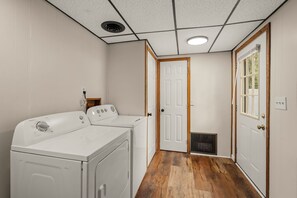 A laundry room with two white front-loading washers and dryers, wooden flooring, a vent, and a door leading to another room. - Lantz Retreat  Hot Tub • Spacious Deck (Lebanon)