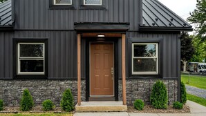 A two-story building with a dark exterior, a brown front door, and a stone foundation. - Lantz Retreat  Hot Tub • Spacious Deck (Lebanon)