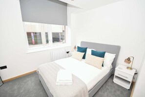 Une chambre moderne avec un grand lit, une table de chevet, une commode, une fenêtre et un radiateur.