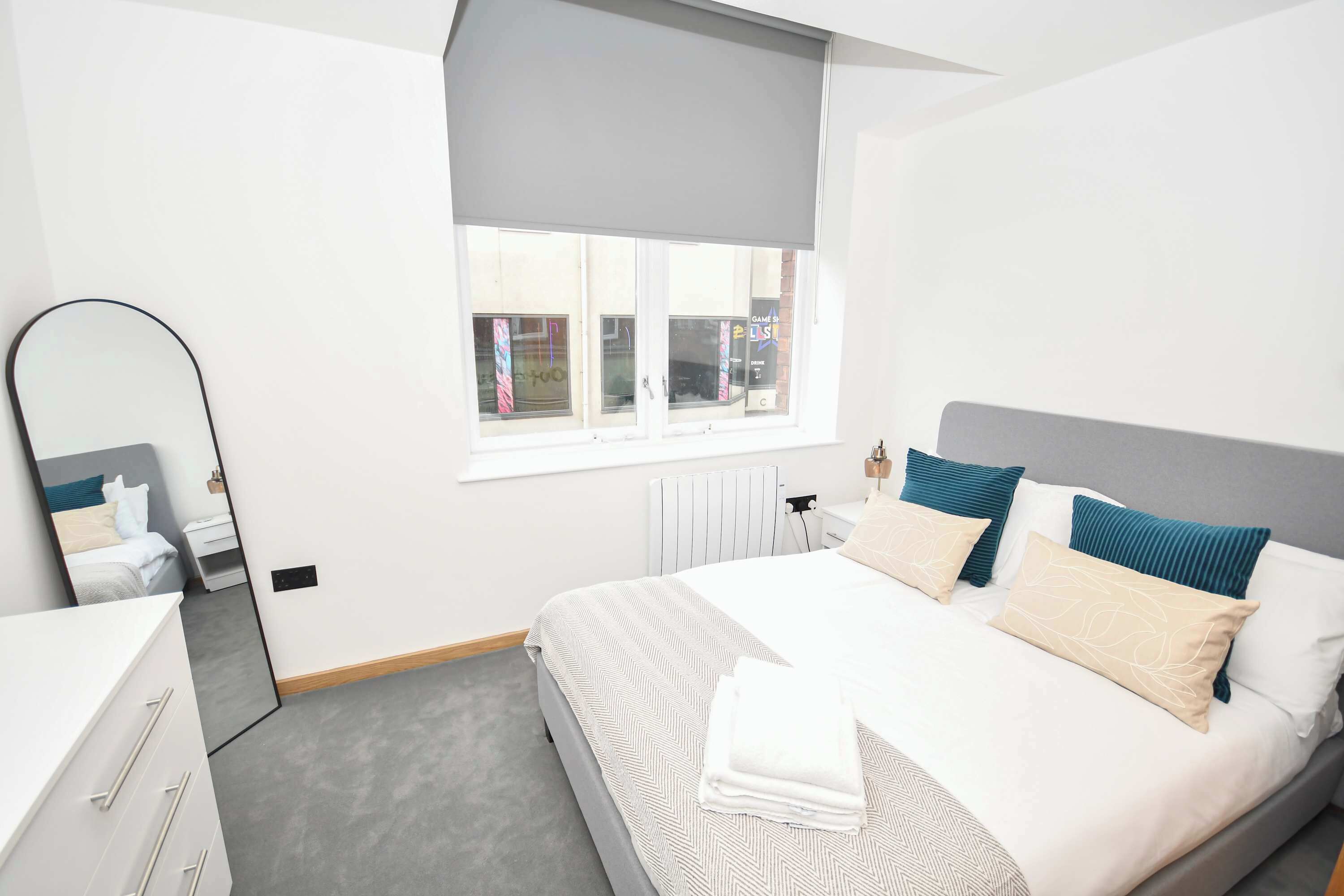 Une chambre à coucher moderne, avec un lit, des tables de chevet, un miroir et une fenêtre donnant sur l’extérieur.