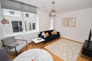 Uma sala de estar moderna com sofá, mesa de centro, rack para TV e uma janela grande.