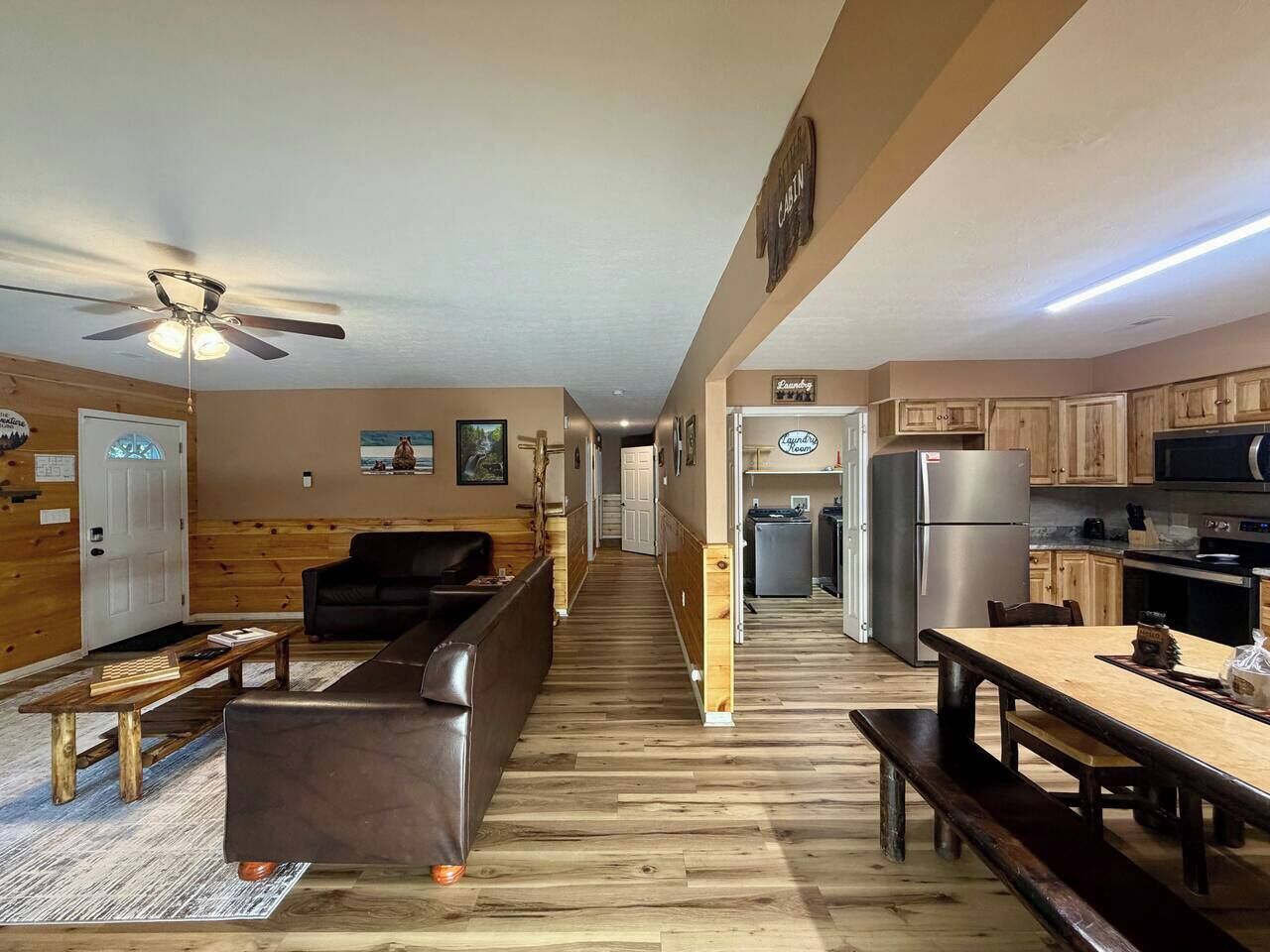A spacious living area with a sofa, a wooden coffee table, and a ceiling fan. A kitchen with wooden cabinets and appliances is visible in the background.