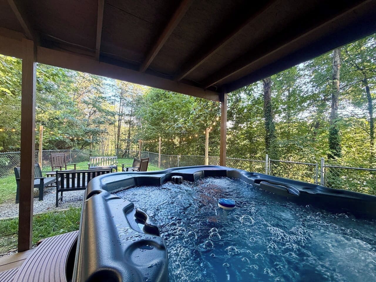 A hot tub under a wooden pergola with a view of a wooded area.