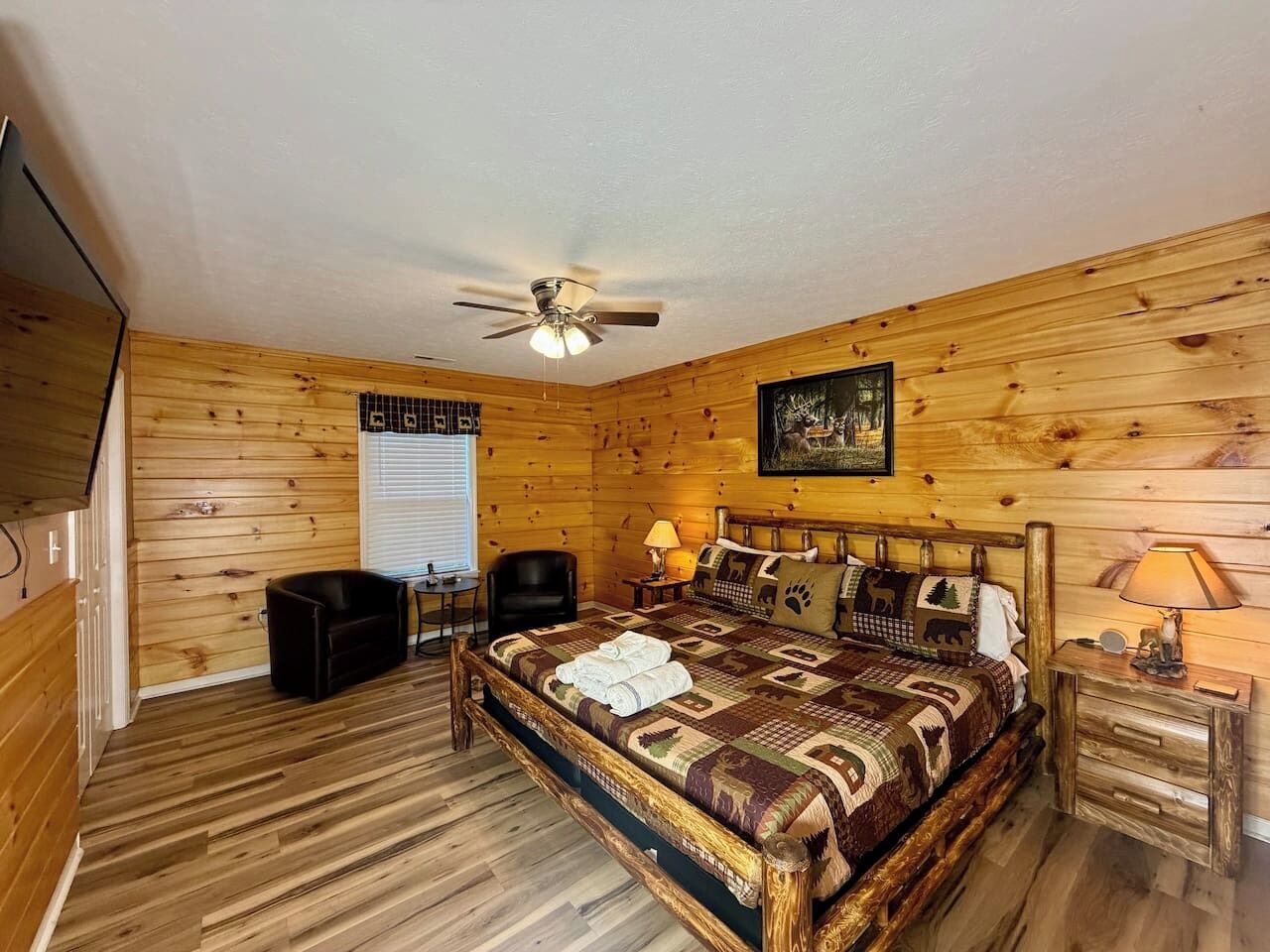 A wooden-paneled room with a bed, a ceiling fan, a desk, and a chair.