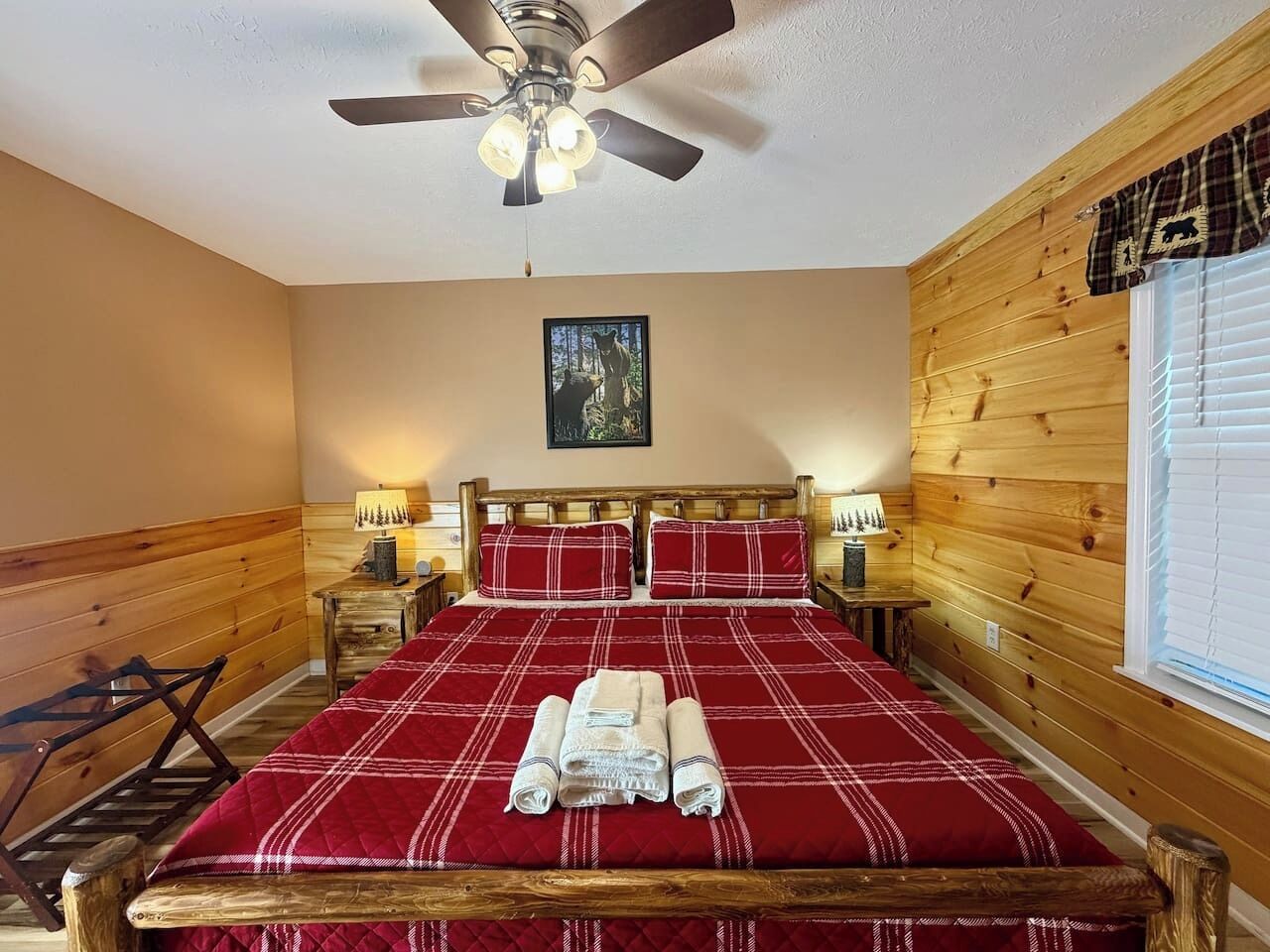 A bedroom with a wooden headboard, a bed with a red and white checkered bedspread, two bedside lamps, and a ceiling fan.