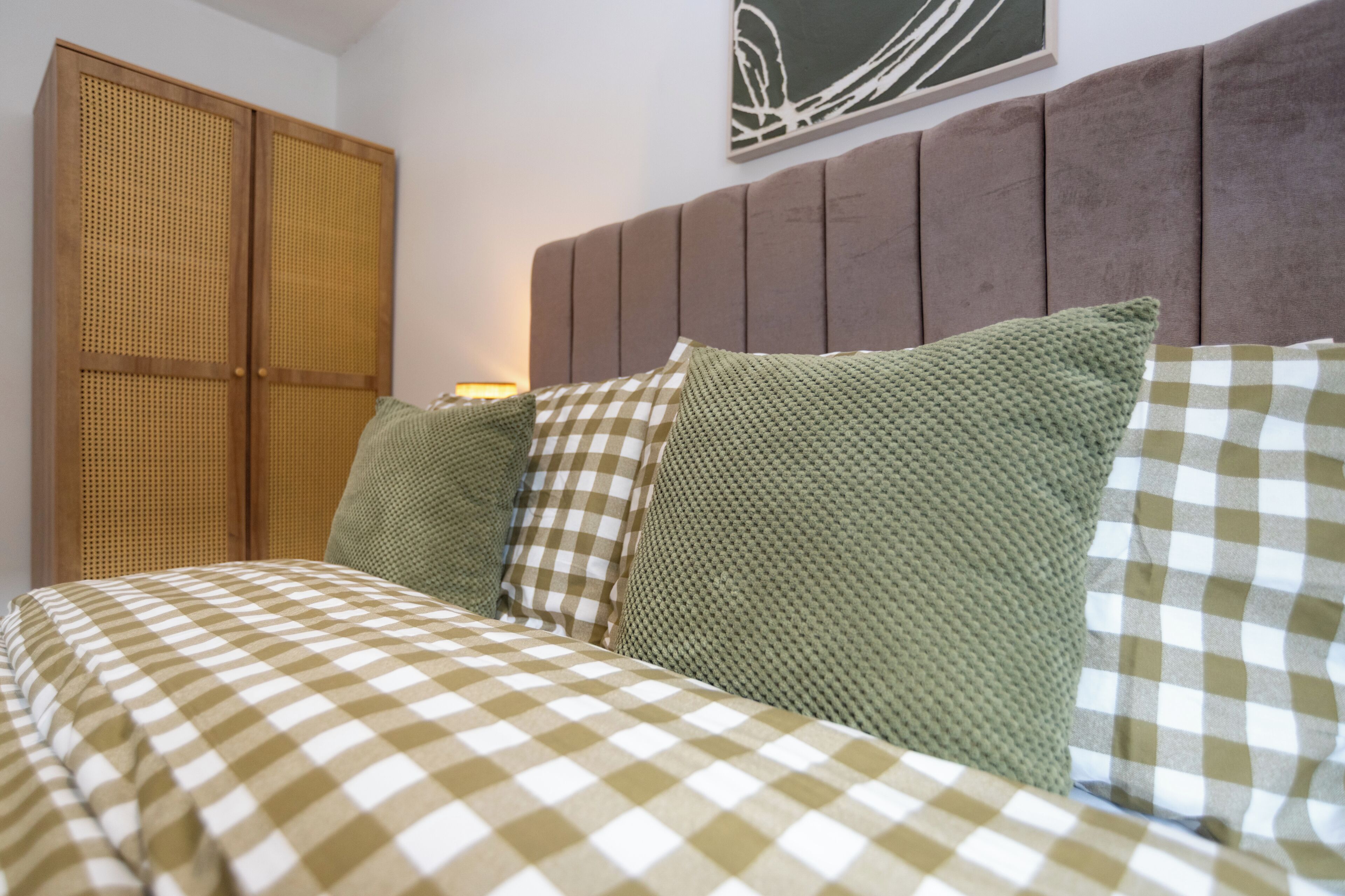 Una cama con ropa de cama a cuadros, un cabecero con panel texturizado y una obra de arte colgada en la pared.