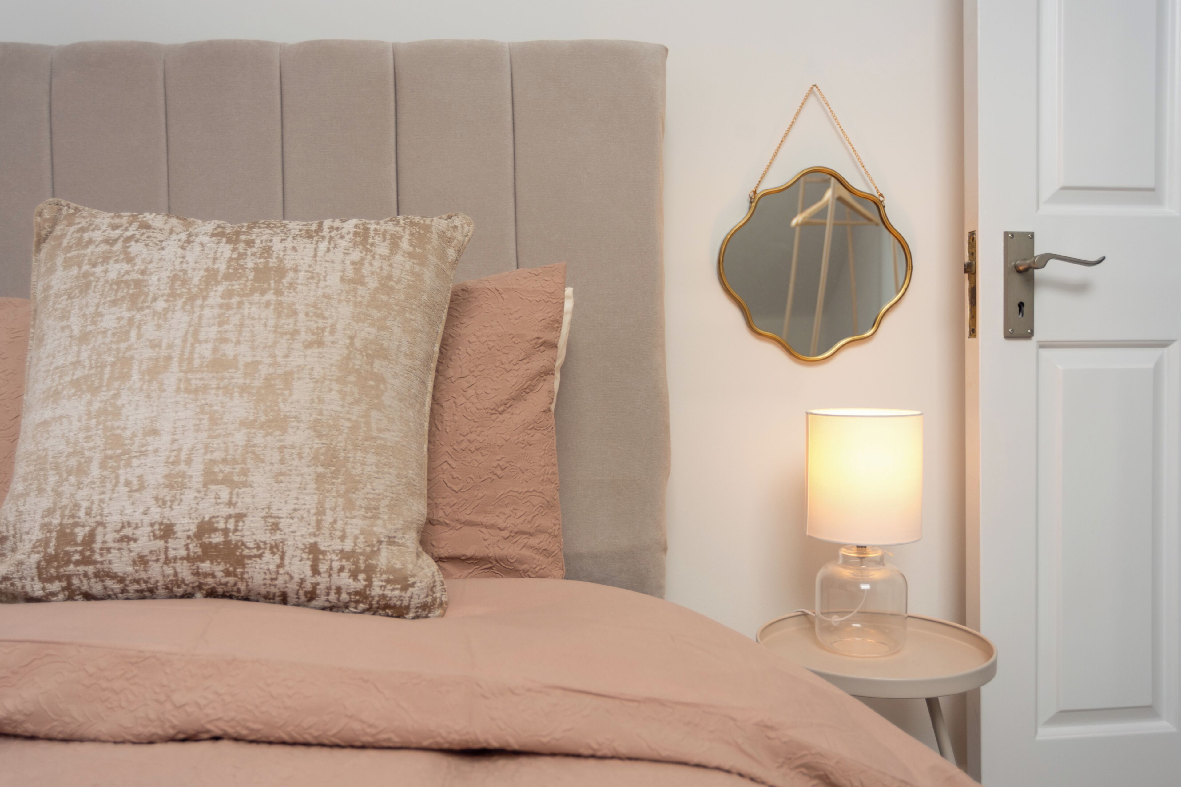 Ein Bett mit Kopfteil, zwei Kissen, ein Nachttisch mit Lampe und eine Tür.