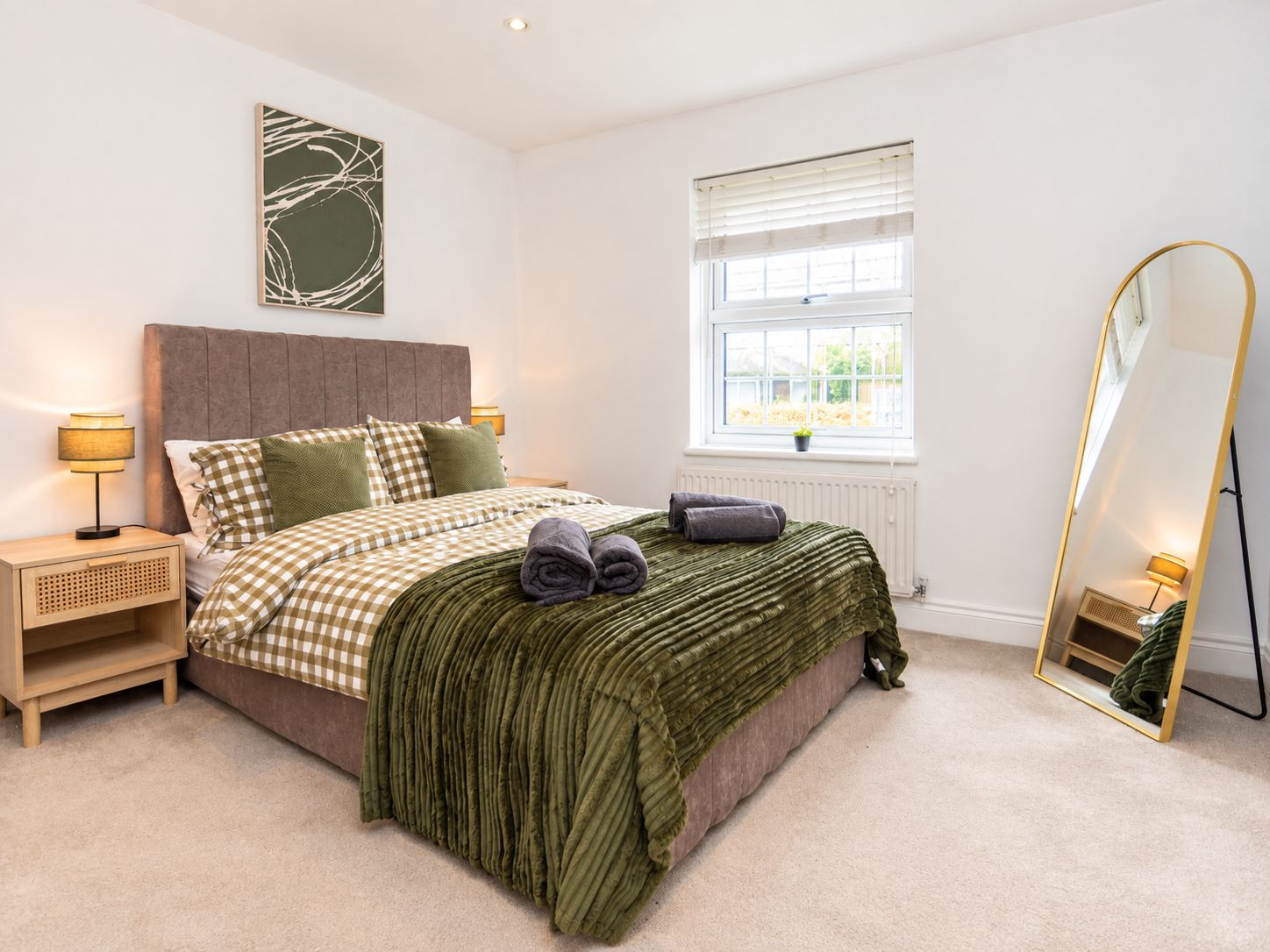 A bedroom with a bed, bedside tables, a window, and a mirror.