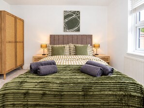 Un dormitorio con una colcha a cuadros, dos lámparas de noche, un armario de madera y una ventana con persianas.