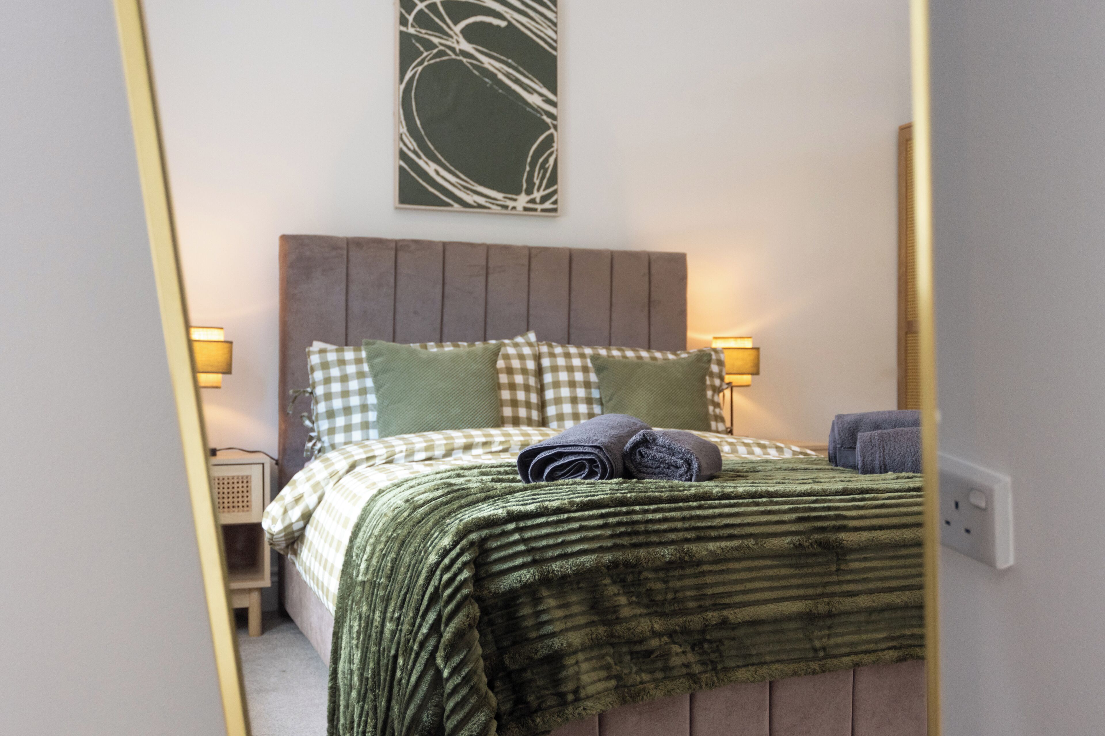 A bedroom with a bed, pillows, a blanket, and a wall-mounted artwork.