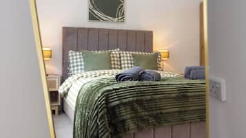A bedroom with a bed, pillows, a blanket, and a wall-mounted artwork.