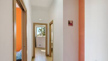 A narrow hallway with wooden flooring, white walls, and a door leading to a room with a patterned bedspread.
