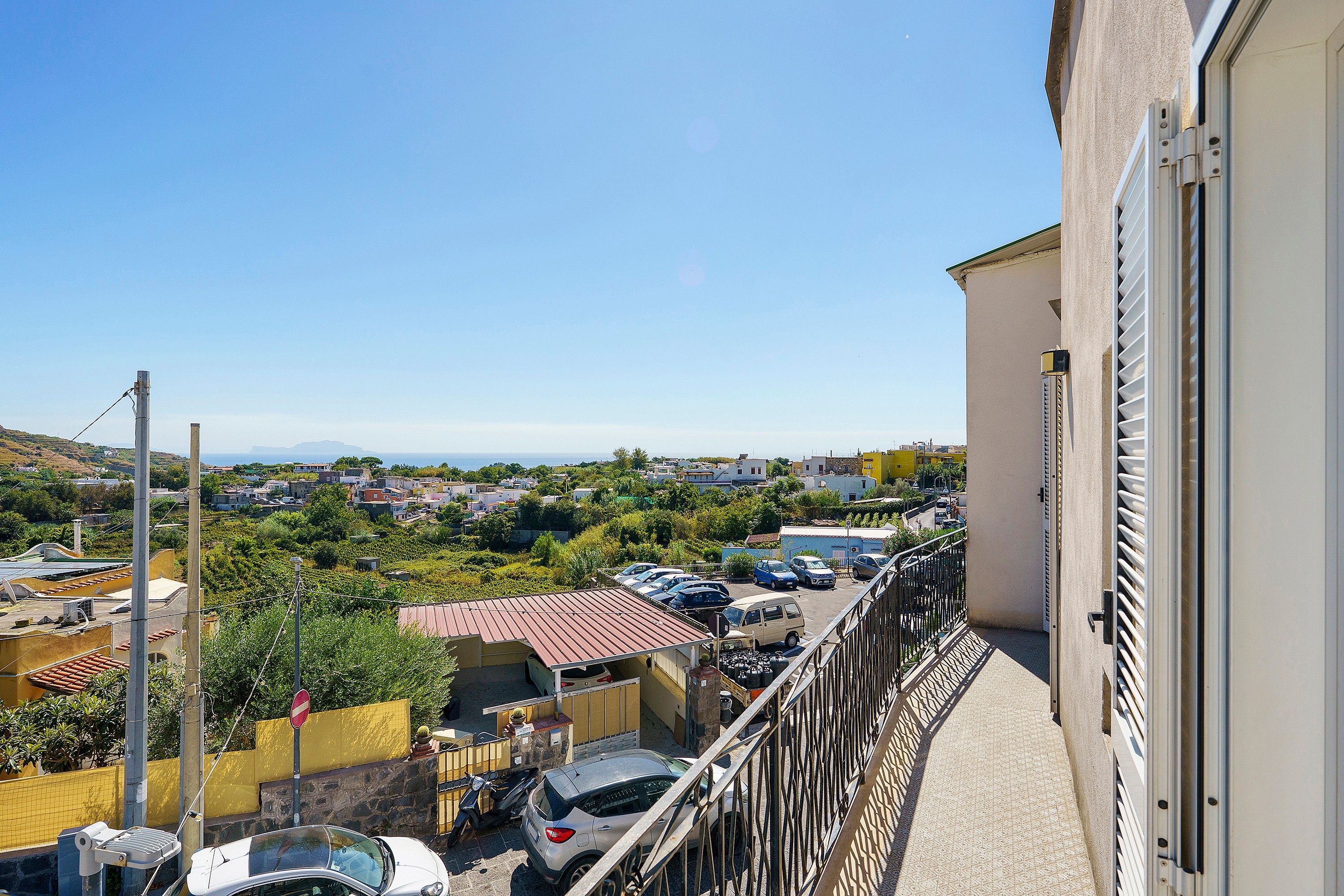 Un balcone con vista su una zona residenziale, un'auto parcheggiata e un edificio con cancello in metallo.