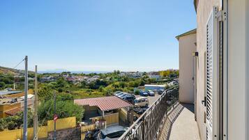 Un balcone con vista su una zona residenziale, un'auto parcheggiata e un edificio con cancello in metallo.