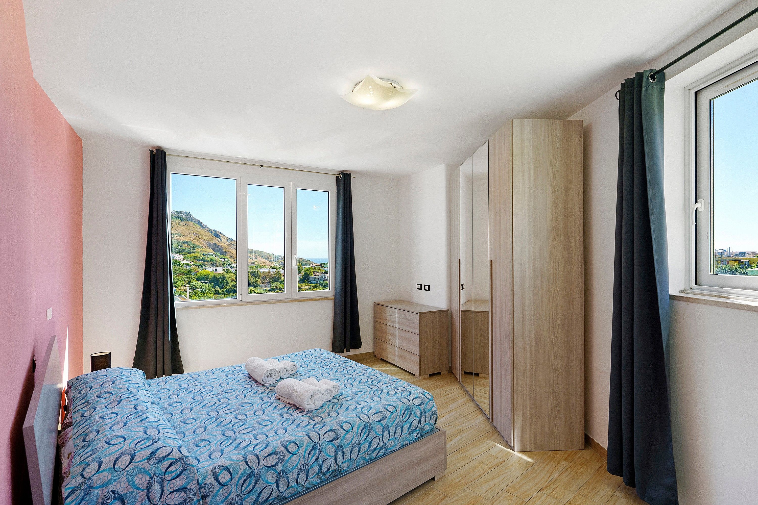 A bedroom with a bed, a wardrobe, a dresser, and a window with a view of a landscape.