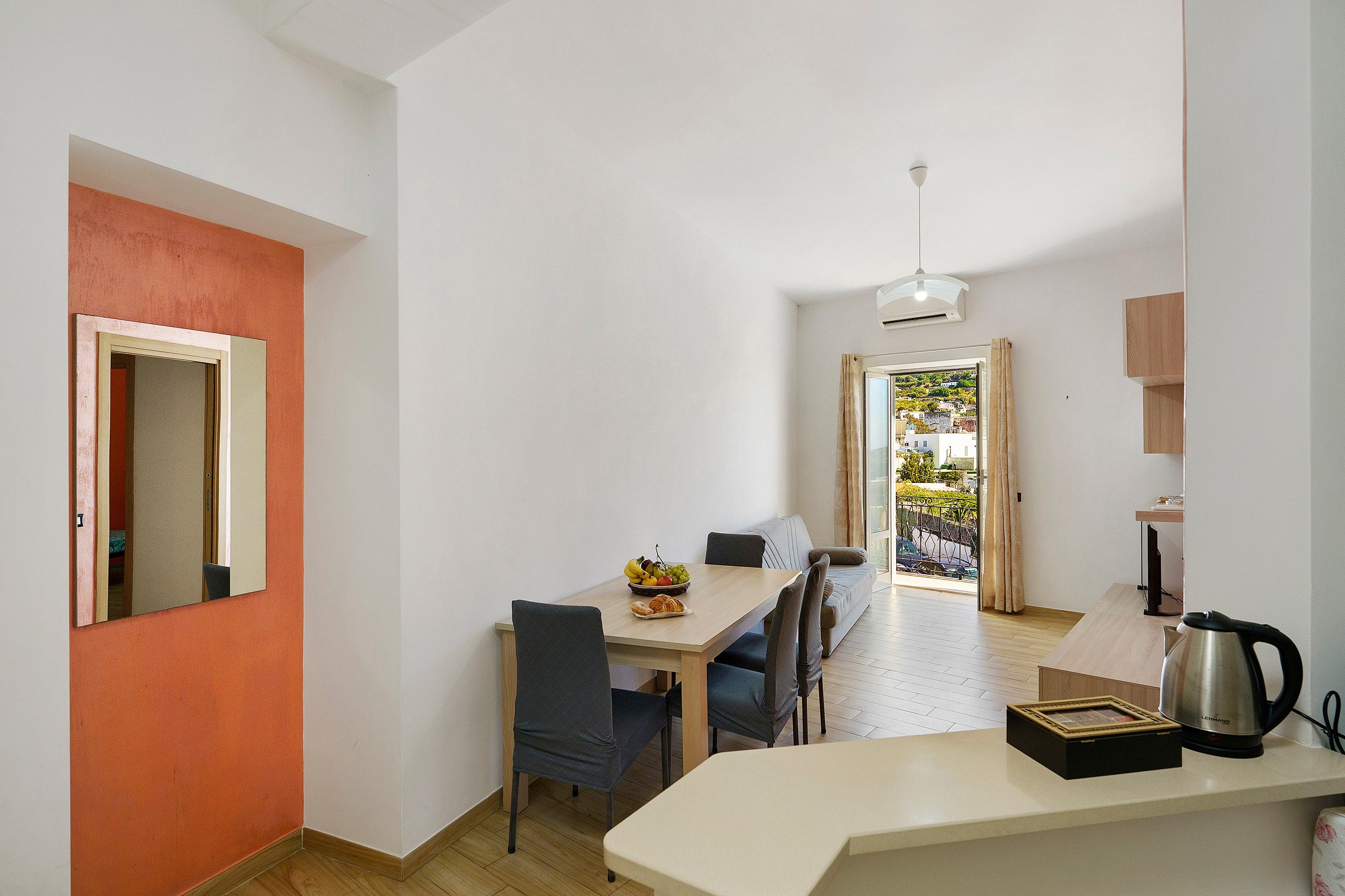 Ett kompakt bostadsutrymme med en matplats, ett litet kök och utsikt genom en dörr.