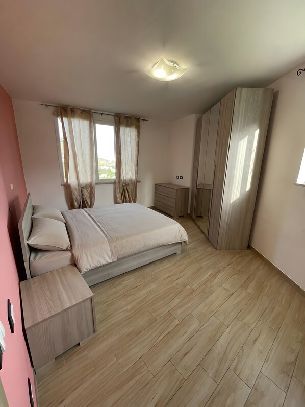 Ein Schlafzimmer mit Bett, Nachttisch, Kleiderschrank und einem Fenster mit Vorhängen.