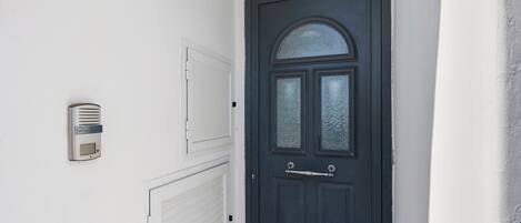 A black door with a glass panel and a handle, a white wall with a light fixture, and a white garage door.