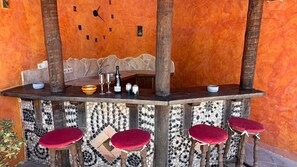 A bar area with a clock, bottles, glasses, and red cushioned stools.