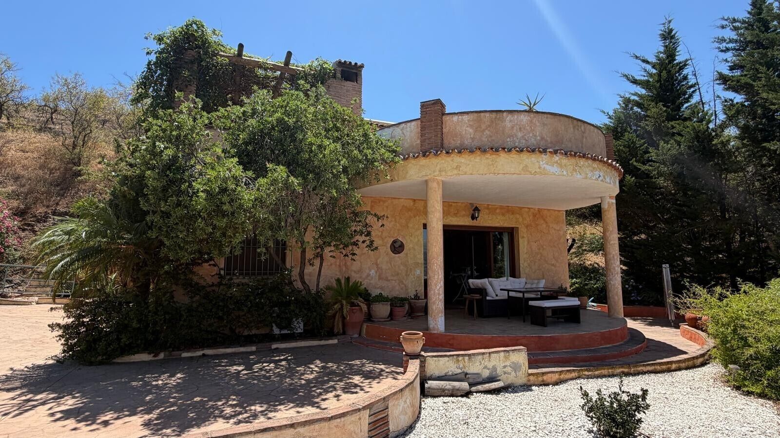 Un edificio circular con un patio cubierto, asientos al aire libre y un jardín con diversas plantas.