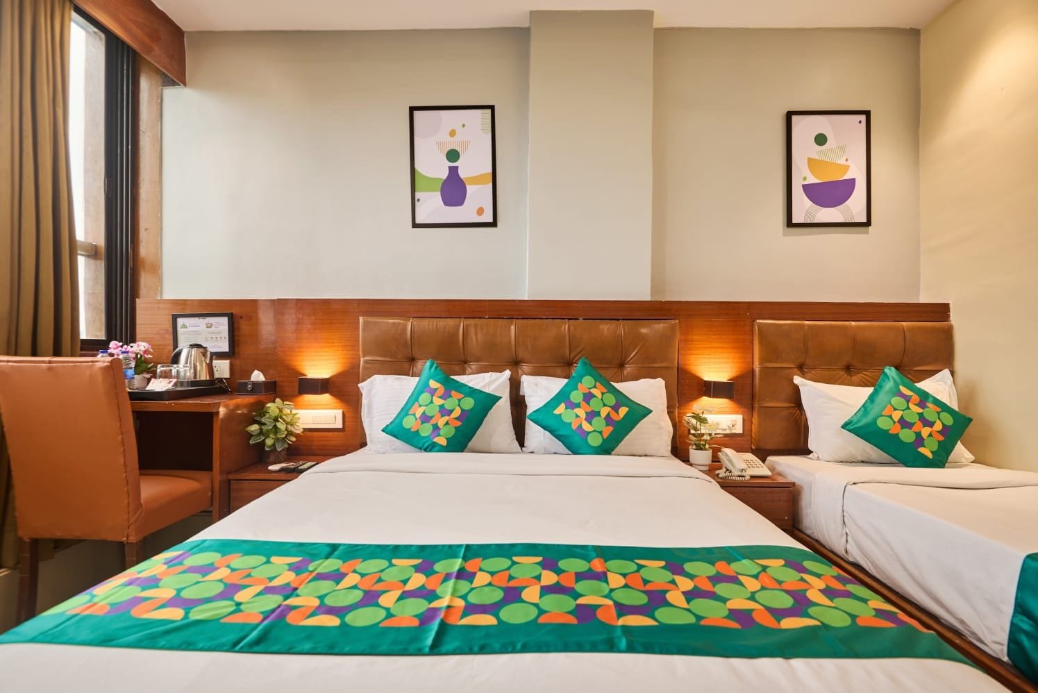 A hotel room with a large bed, two bedside tables, a desk, and a chair. There are two framed pictures on the wall.
