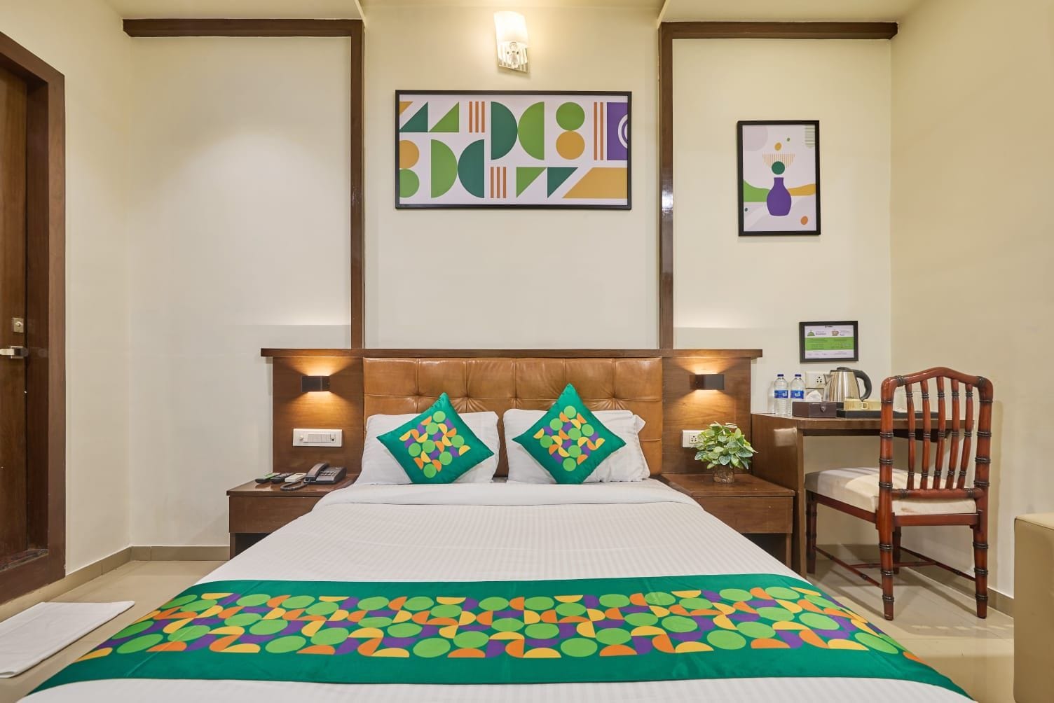 A hotel room with a bed, two bedside tables, a desk with a chair, and artwork on the walls.