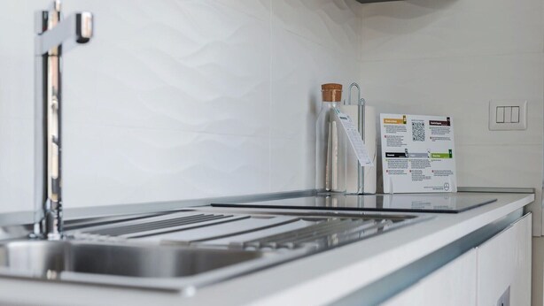 Cozinha moderna com pia de aço inoxidável, torneira e dispensador de papel com cardápio.
