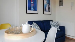 Uma sala de estar moderna com uma mesa redonda branca, um sofá azul e duas fotos emolduradas na parede.