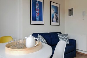 Un salon moderne avec une table ronde blanche, un canapé bleu et deux tableaux encadrés accrochés au mur.