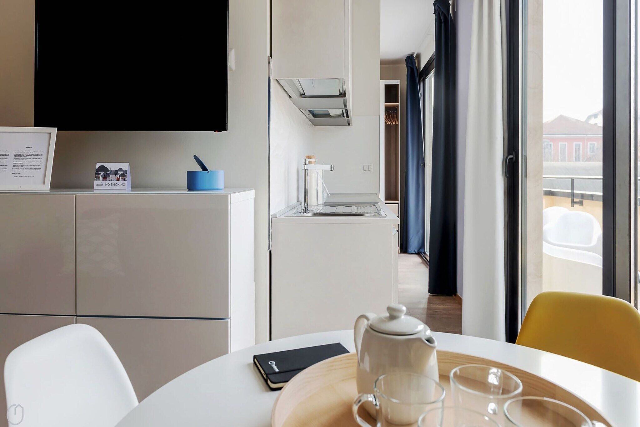 A hotel room with a dining table, a kettle, and a smartphone.