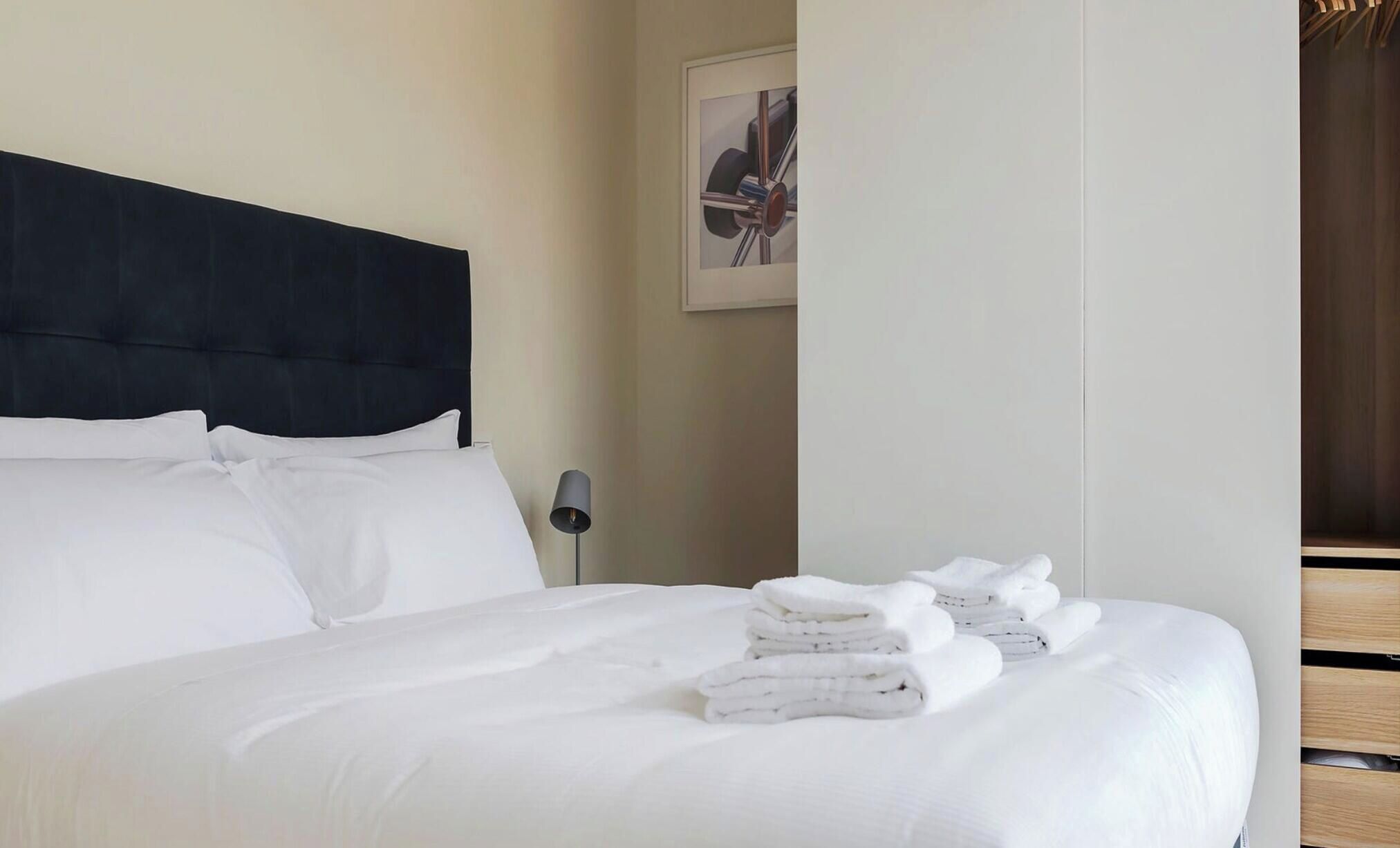 A neatly made bed with white linens and a stack of folded towels.